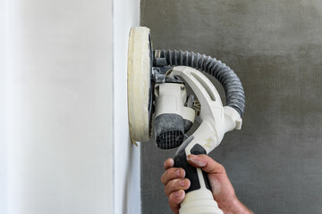 Painter polishing and sanding wall surface after putty for painting in new apartment. © Natallia