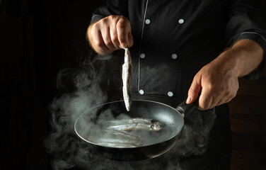 Frying capelin in a frying pan. Small crispy fish are prepared by the hands of the chef. Menu for a restaurant or hotel