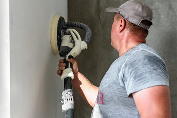Painter polishing and sanding wall surface after putty for painting in new apartment.