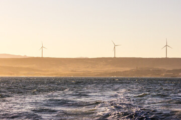 Wind turbines among the dunes of the Namib desert, along the coast in Namibia at dawn.