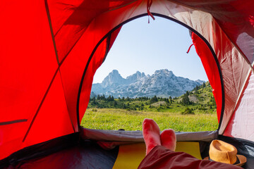 Relaxing in the tent with a beautiful morning view of a green meadow with rocky mountain peaks in the background