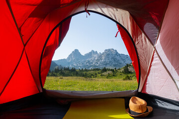 A beautiful view from the tent of a green meadow with rocky mountain peaks in the background