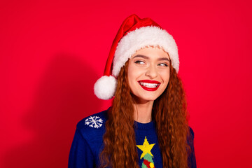 Photo of charming positive girl wear unly print sweater santa hat celebrating xmas looking empty space isolated red color background
