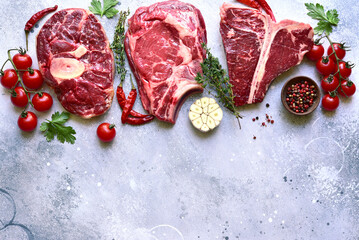 Different types of raw marbled beef steaks : T-bone, ossobuco, spider and rib eye with ingredients for cooking . Top view with copy space.