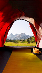 A beautiful view from the tent of a green meadow with rocky mountain peaks in the background