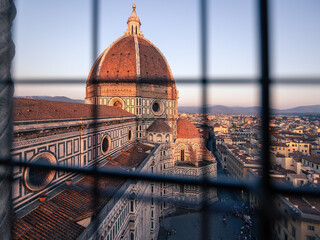 Florence Duomo cathedral roofs of historic city at sunset through lattice of bell tower window,...
