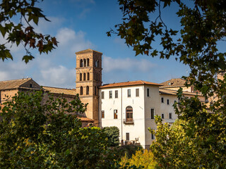 View through vegetation to medieval buildings and renaissance bell tower on sunny day, Rome, Italy