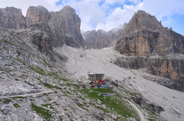 Rifugio Silvio Agostini in the middle of amphitheater of rock, on the wild slopes of Brenta Dolomites. Starting point for excursions and climbing. Breathtaking mountain landscape. Clouds in the sky.