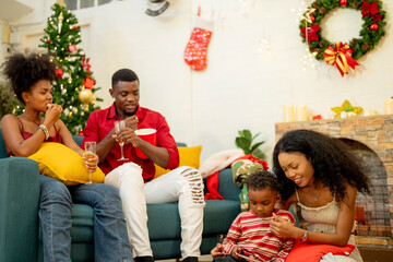 A family enjoying a cozy Christmas evening at home. The group gathers around the Christmas tree, sharing laughs and stories. The warmth of the festive season is felt as they relax and bond together.