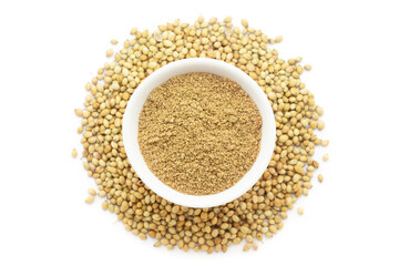 A bowl of Organic Coriander (Coriandrum sativum) powder, placed over a heap of whole Coriander seeds. Isolated on a white background.