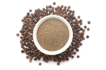 A bowl of Organic Black pepper (Piper nigrum) powder, placed over a heap of whole Black pepper. Isolated on a white background.
