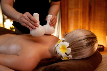 Hot herbal ball spa massage body treatment, masseur gently compresses herb bag on woman body....