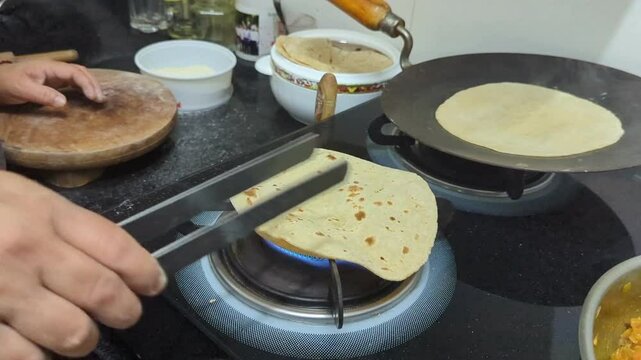 woman's hand cooking a phulka roti over a gas flame on a stove with expert skill, causing it to puff up and expand into a fluffy, delicious flatbread in the kitchen