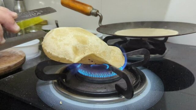 woman's hand cooking a phulka roti over a gas flame on a stove with expert skill, causing it to puff up and expand into a fluffy, delicious flatbread in the kitchen