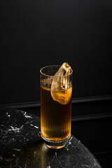An alcoholic cocktail in a highball glass garnished with dried pear slice served on ice in a bar