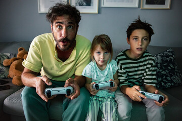 Father playing video games with his son and daughter at night in the living room