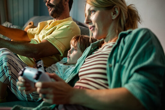 Young family playing video games at night on the couch in the living room at home