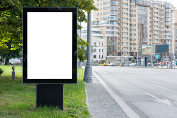 White blank vertical billboard in the city. Green lawn, multi-storey building. Mock-up.