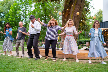 Fototapeta premium Cheerful dance party outdoors, featuring individuals of different ages enjoying the festive ambiance under illuminated string lights. They are dancing swing dance in summer city park
