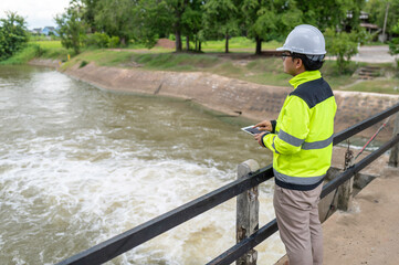 A engineering doing his checking routine. He is wearing hard hat and engineer uniform.Standing by the rail by the dam.Monitor water levels from the heavy rain that has been falling for several days.