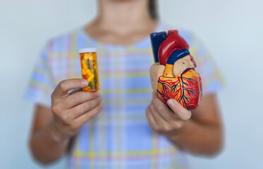 Person holding a heart model in one hand and a prescription bottle in the other, highlighting health 