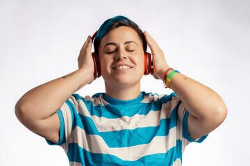 Joyful non-binary person with blue hair enjoying music through red headphones on white background