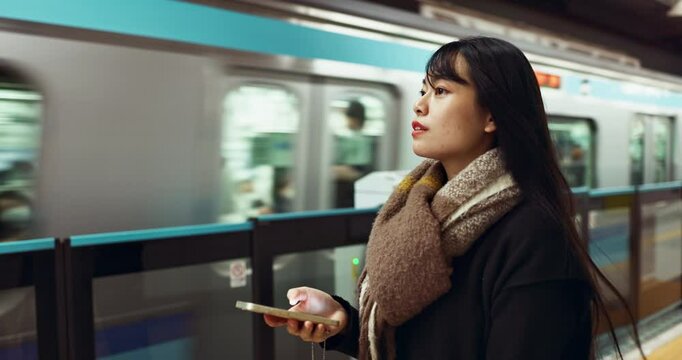 Japanese woman, phone and train station for travel with app, waiting and happy for metro transportation. Girl, smartphone and happy for commute with locomotive for journey, adventure or web in Tokyo