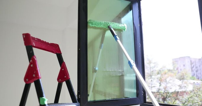 Cleaning a window using a scraper and a ladder