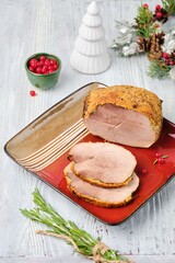 Cold appetizer or hot dish, Christmas ham from pork leg on red square plate on light wooden background. Festive dishes.
