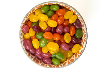 Colorful jelly beans in a variety colors in a round bowl with orange pattern isolated on a white background