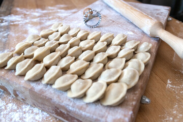 The raw dumplings were placed on a wooden cooking board. Next to it is a rolling pin for rolling out the dough and a tool for cutting the dough. Modeling dumplings by hand.
