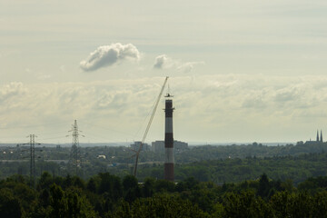 Aerial drone view of demolition of chimney, excavator working on smokestack. Small excavator destroying a tall chimney. Work on top of the chimney. A suspended excavator on a crane destroys a chimney