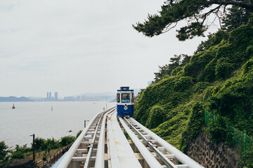 A scenic cable car travels along a hillside overlooking the coastline of Haeunde Blueline Park on a cloudy day