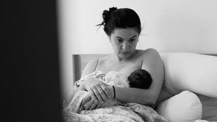 Mother breastfeeding her newborn baby while sitting in bed. Emotional and serene depiction of the...