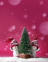 Two little snowmen in caps with Christmas tree on snow in the winter. Background with a funny snowmen. Christmas card.