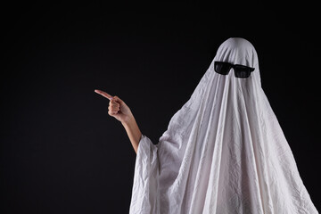 Person in costume of ghost pointing at something on dark background with space for tex