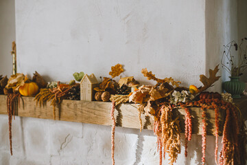 Stylish decoration of fireplace with pumpkins, autumn leaves, nuts, candle on rustic wood in modern farmhouse living room. Autumn decor on fireplace mantel. Thanksgiving and Halloween