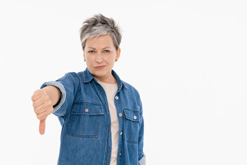 Mature adult woman showing thumb finger down as refusal sign. Studio portrait of unhappy dissatisfied lady expressing dislike isolated on white background copy space. People emotions concept