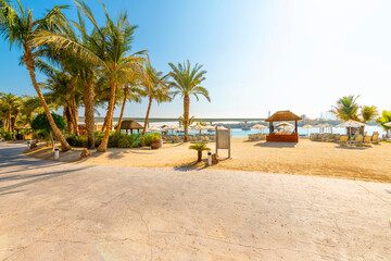 Lounge chairs, palm trees and huts along a sandy beach and resort on Palm Jumeirah island, on the Arabian Gulf at Dubai, United Arab Emirates.