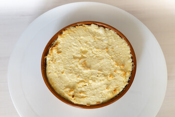 Vegan cheesecake cake close-up on white wooden table. Top view on whole round cheesecake in brown plate on light background. Homemade cooking, cheese cream tart