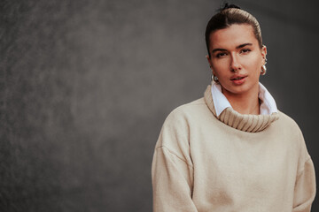 Fashionable woman in beige sweater on city street looking at camera.