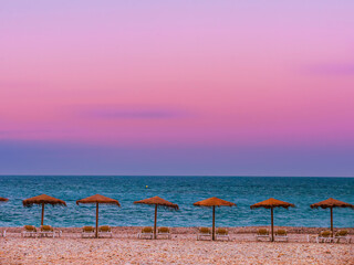 Straw beach umbrellas lined up on a shore against the sunset sky