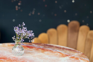 A bouquet of dried gypsophila in a small glass vase on a marble table against a dark blue background in a restaurant.