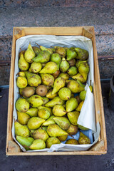 Green pears for sale in a crate displayed near the window of a vegetable shop.