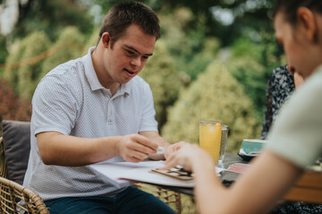 A young man with Down syndrome shares a joyful moment with friends at an outdoor cafe, highlighting inclusivity and friendship in a warm, natural setting.