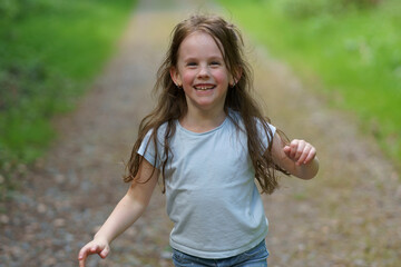 Obraz premium Little beautiful girl on the background of the road in the park. Happy childhood concept outdoors