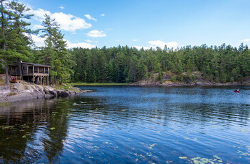 Water View of a Rustic Cottage Along the Shore of Pine Cove in French River Provincial Park and People Paddling in Their Canoe