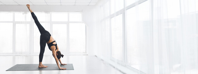A woman practices yoga in a spacious studio, demonstrating a challenging pose with one leg extended...