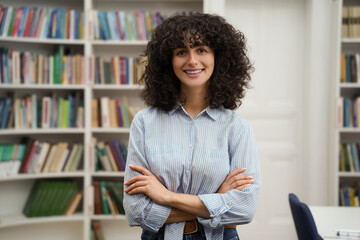 Curly-haired pretty young woman standing on the bookshelves background