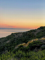 Vibrant green hillside overlooking pink and orange sunset over the ocean on west coast